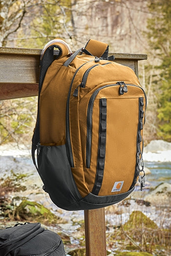 A duck brown Carhartt® 25L Ripstop Backpack hanging from a table hook.